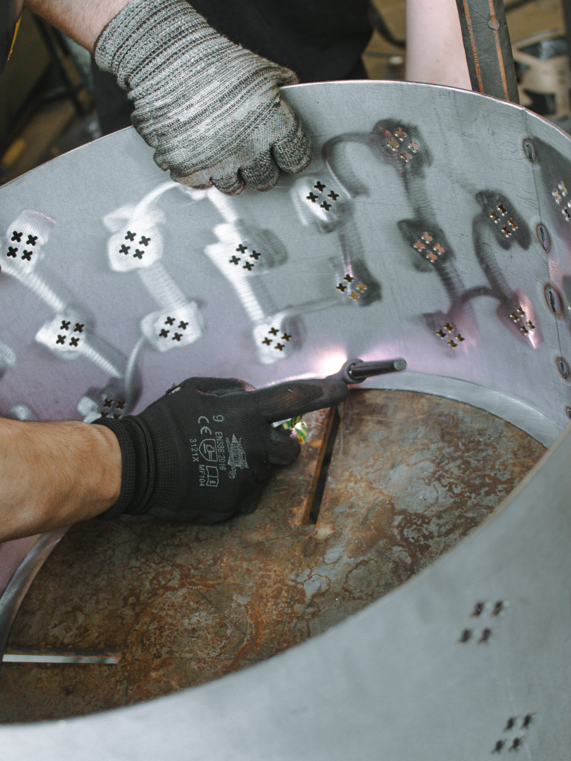 Assemblage manuel d’une structure métallique incurvée, perforée de motifs en croix, en atelier de fabrication de luminaires sur mesure