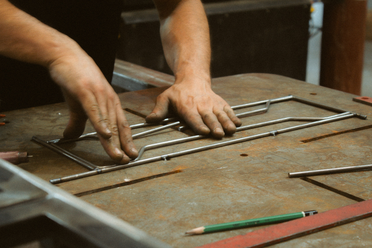 Artisan façonnant à la main des tiges métalliques sur un établi, préparation d’une structure de luminaire sur mesure.