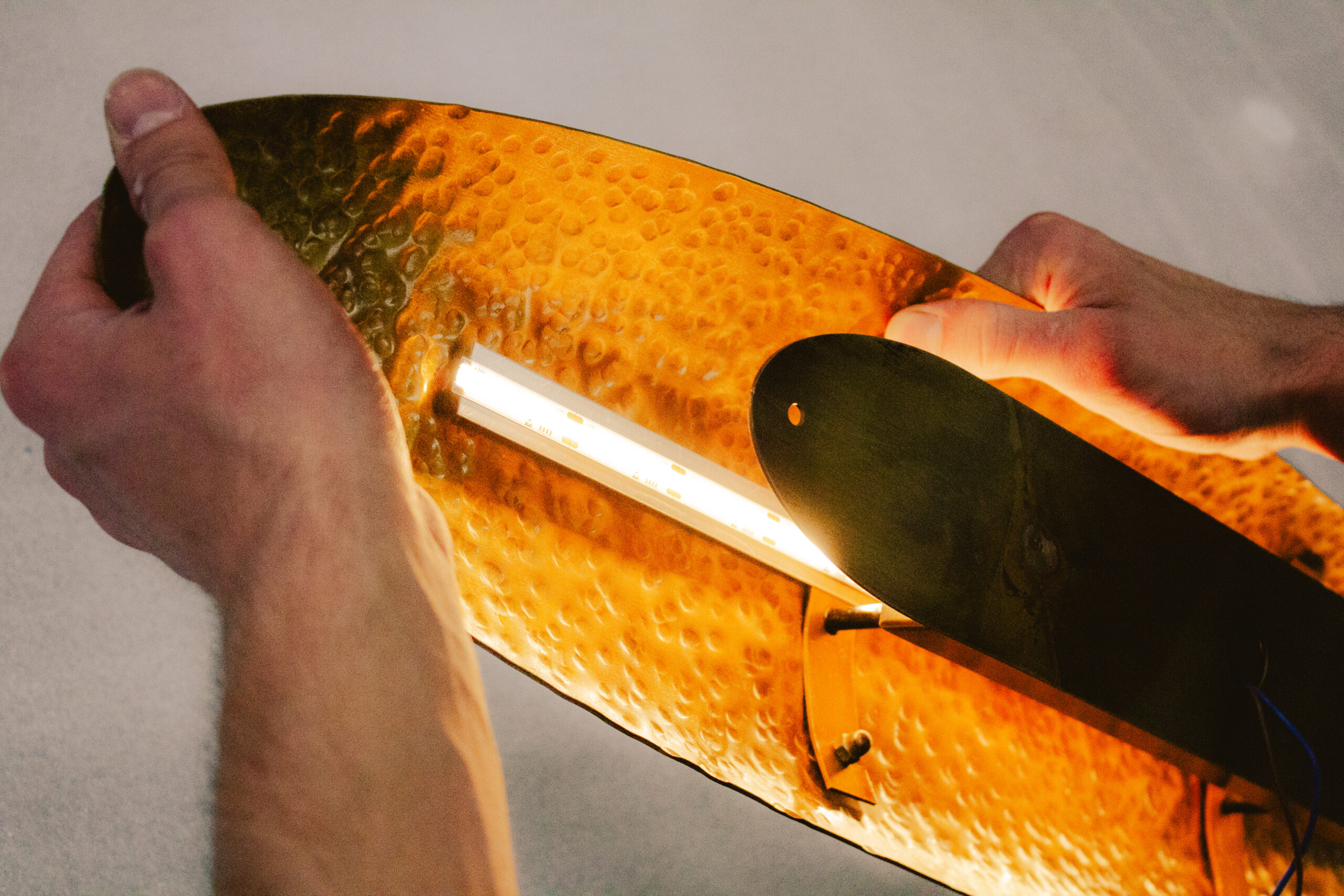 Montage manuel d’une applique murale artisanale en laiton martelé avec éclairage LED intégré, mettant en valeur la texture du métal et le travail de précision