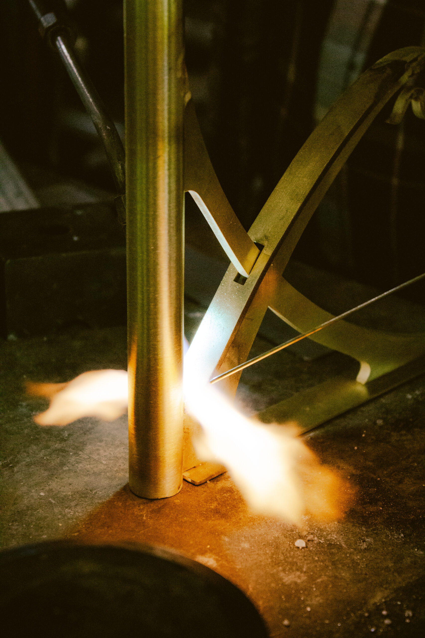 Brasage au chalumeau d’un luminaire en laiton dans un atelier artisanal, capturant la flamme vive et la précision du geste du fabricant