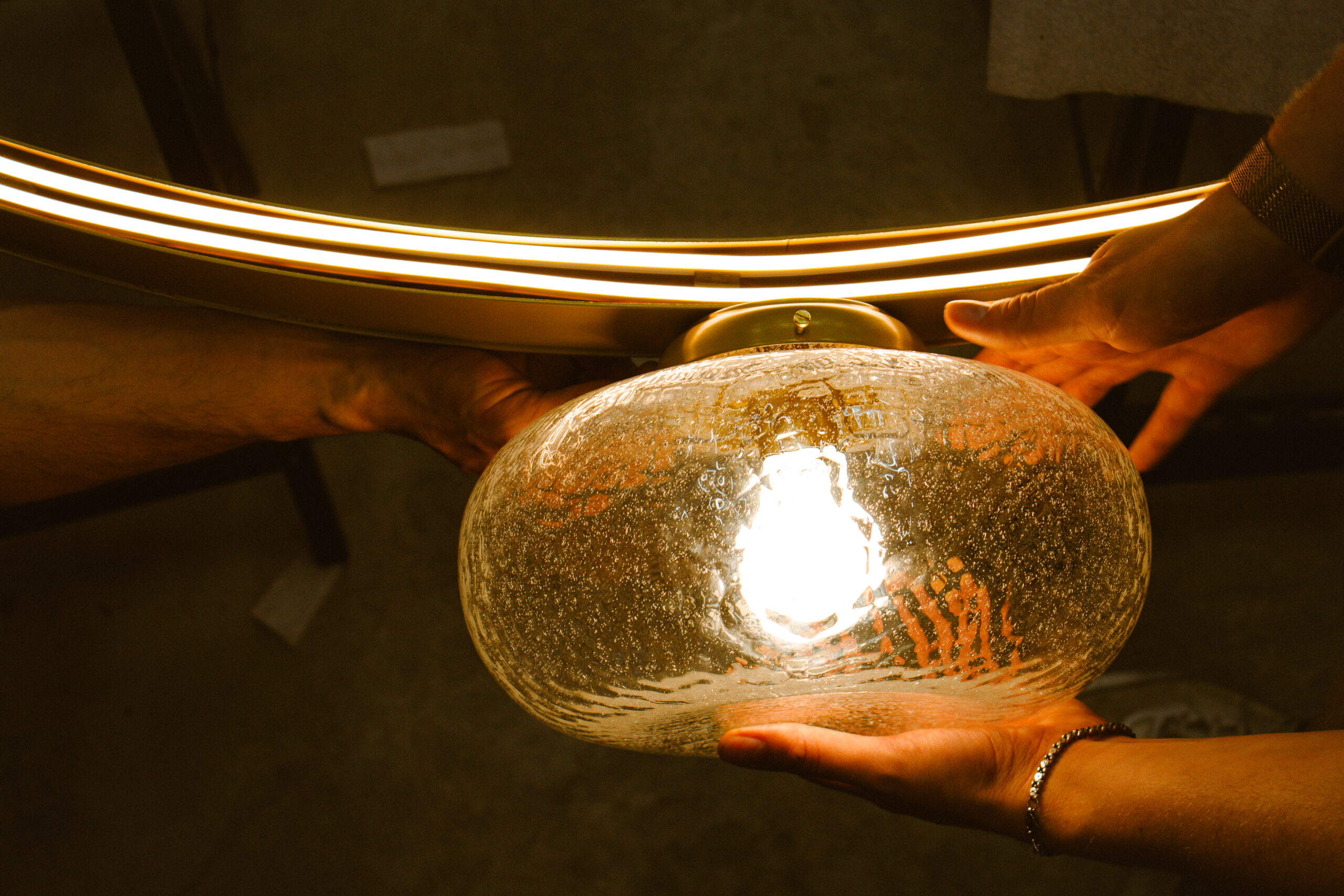 Installation d’un globe en verre soufflé à la main sur une suspension LED en laiton, mise en lumière d’un luminaire design haut de gamme fabriqué artisanalement