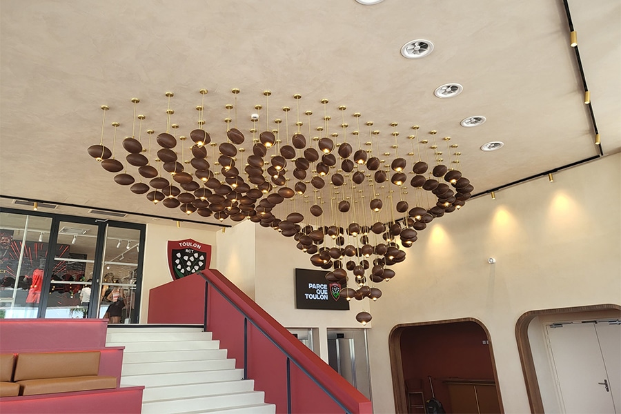 Installation lumineuse sur mesure en forme de nuée de ballons de rugby, lustre design suspendu pour hall du stade de Toulon