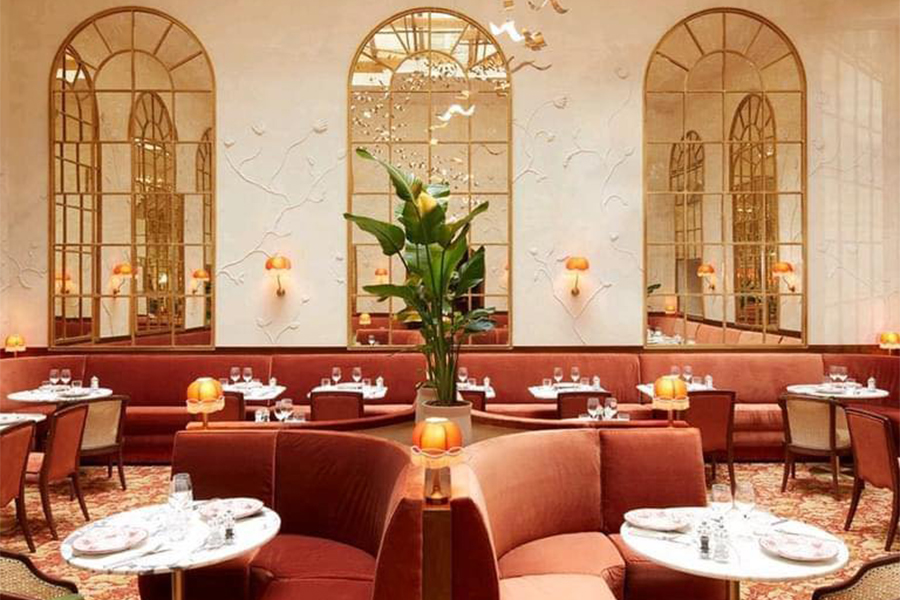 Salle de restaurant élégante avec banquettes en velours rouge, miroirs cintrés muraux, luminaires dorés et ambiance chaleureuse art déco