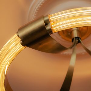 Gros plan sur un luminaire circulaire en laiton et tubes lumineux incurvés, suspendu sous une rosace de plafond en plâtre décoratif